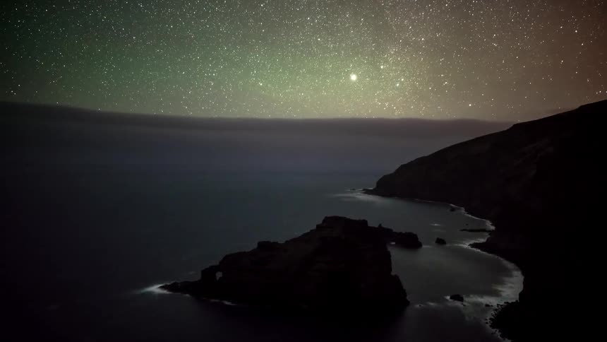 Silhouette of seaside mountains with low clouds passing in a starry night sky