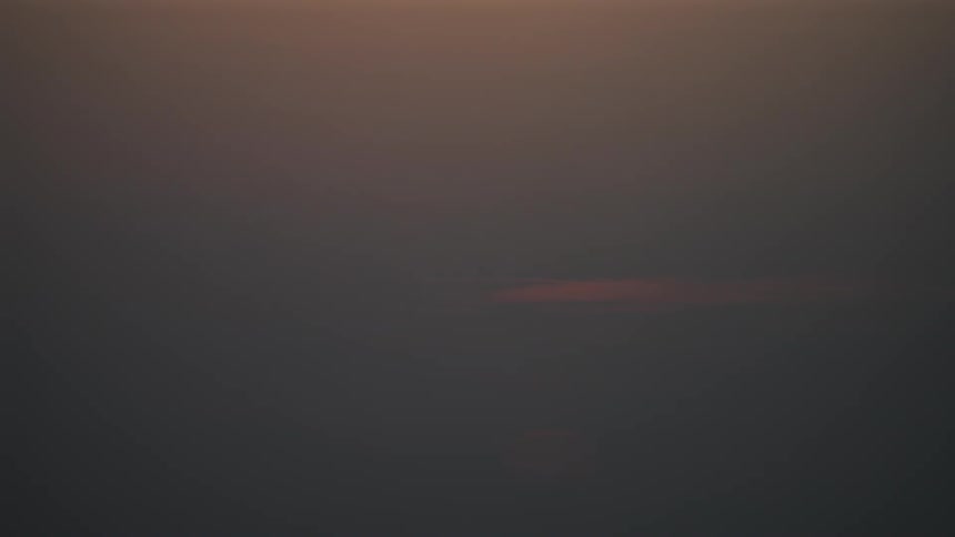 The sun sets behind wispy clouds