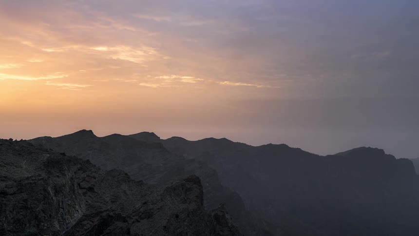 Clouds move over mountains as the sun rises