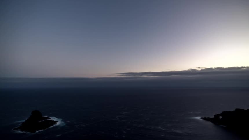 Waves crash against small rocky islands as the sun begins to rise