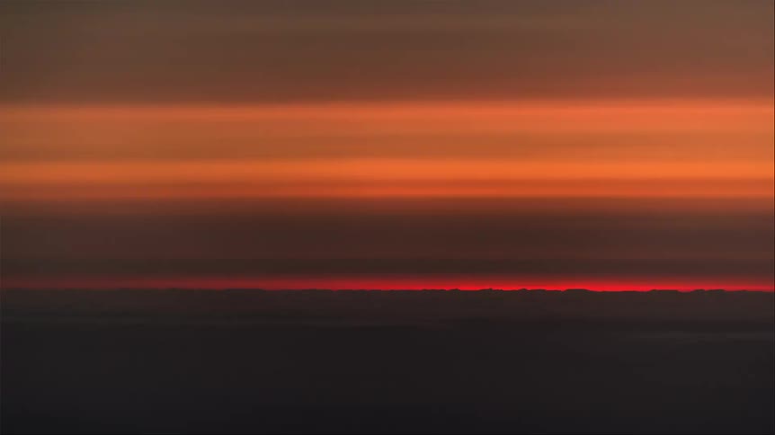 Landscape of a reddish sky darkening with the sun setting on the horizon above a sea of clouds