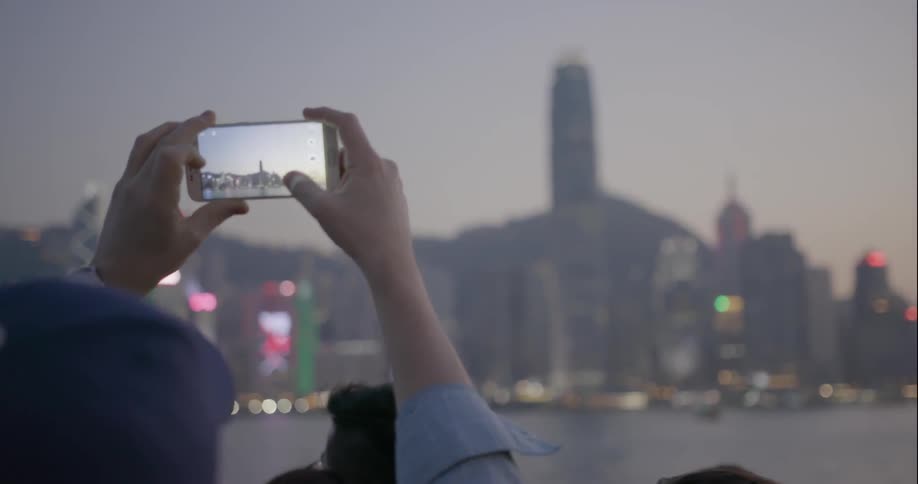 Person using cell phone to photograph building in city