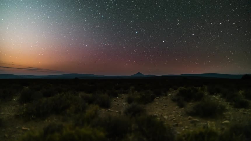 Clouds float over a sparse plain and mountains on the horizon
