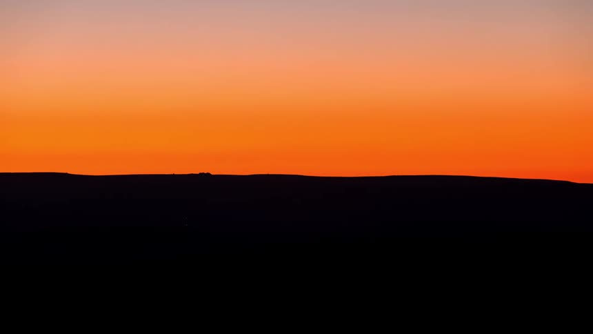 Time lapse of the sun setting on an orange sky over a landscape