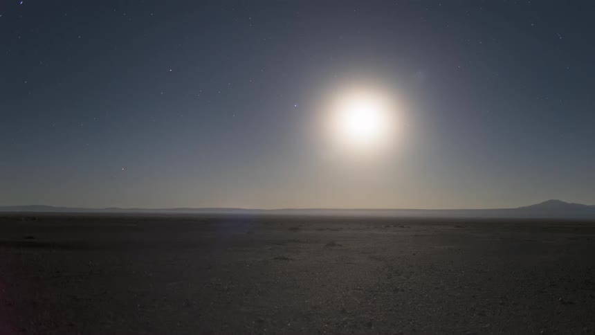 The sun sets over a mountain range and desert and the stars come out at night