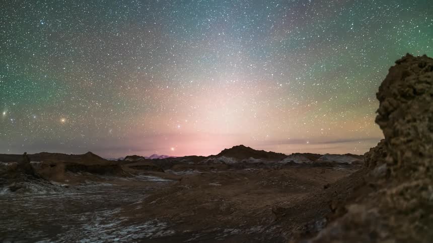 Starry sky with the moon on the horizon on a rocky terrain