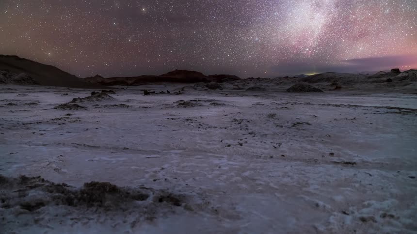 Starry sky with clouds passing over mountains with the ground covered in snow