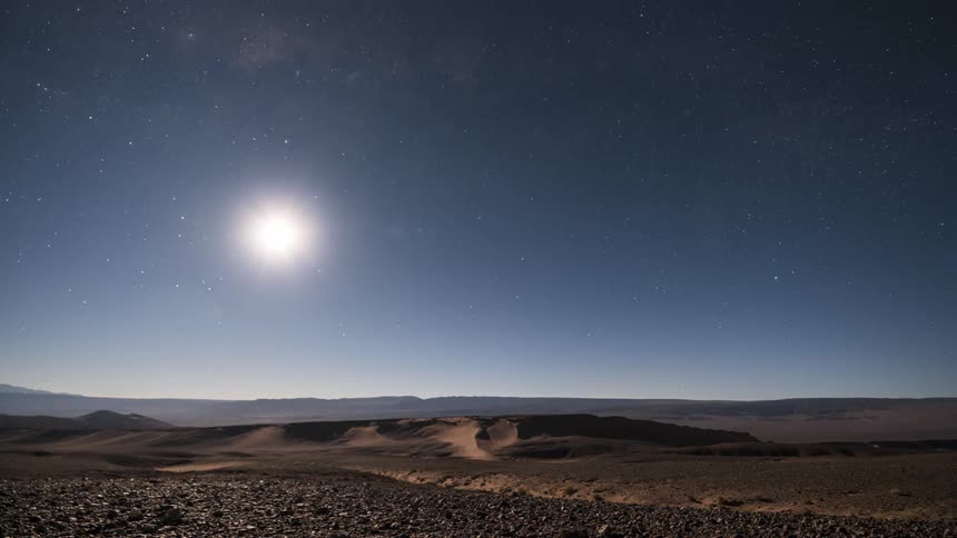 Panorama of a desert floor with the sun setting and stars emerging