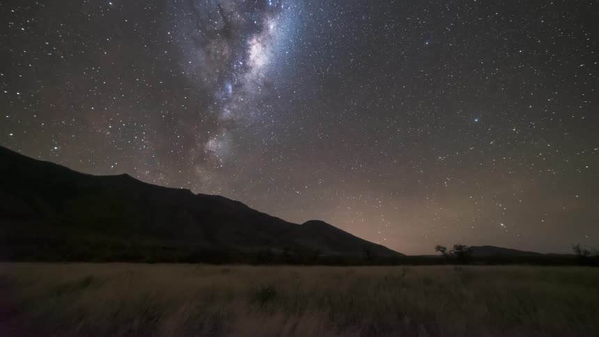 Light emerging from behind the mountains obscuring the starry sky