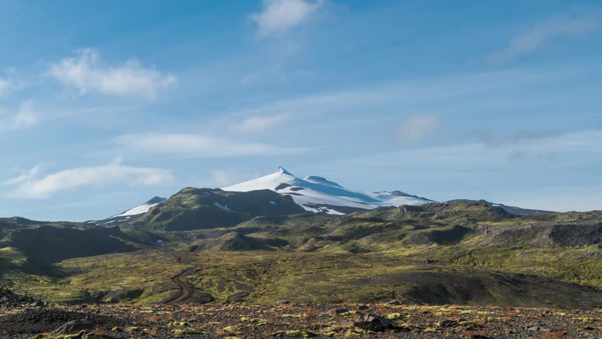 Time lapse of clouds rolling over a mountainous landscape with a peak covered in snow