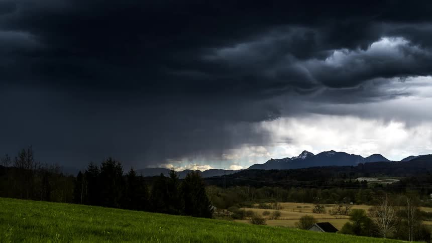 Storm of black clouds above a field and mountains
