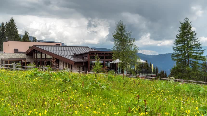 A modern mountain lodge nestled amidst lush greenery and wildflowers a mountain range in the distance