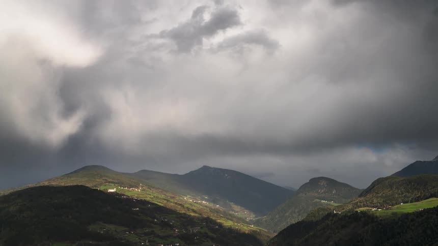 Landscape of greenish mountain ranges with dense black clouds passing by