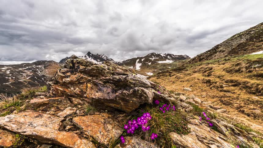 Landscape of rocks on hills surrounded by snowy mountains on a cloudy day