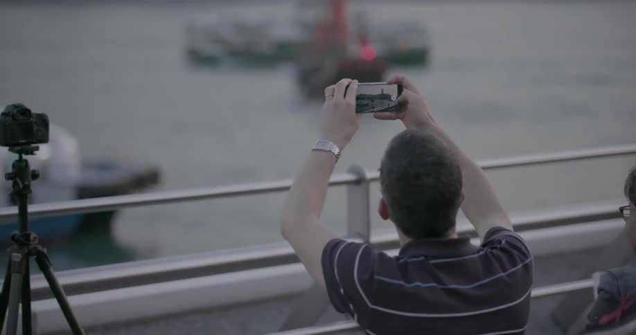 Man taking pictures of ships passing along a river with his smartphone