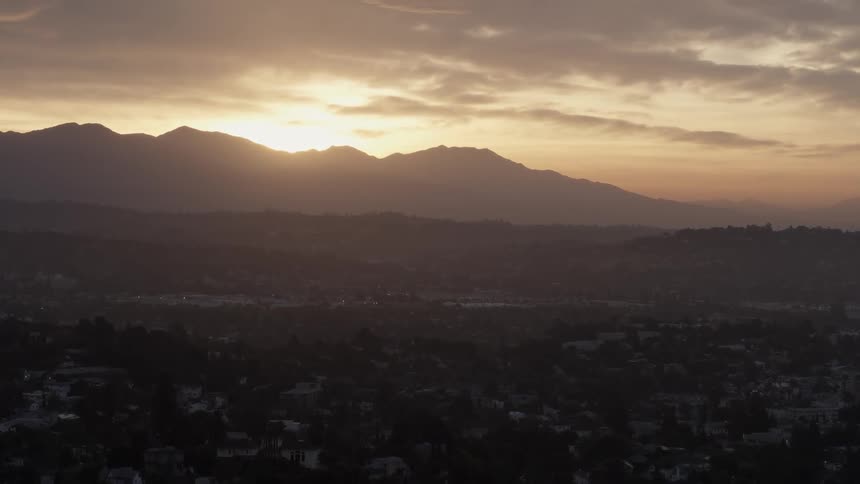 The sun peeks out over the mountains in the distance overlooking a town