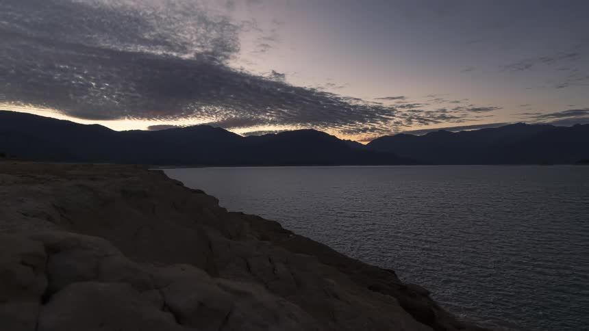 Time lapse of clouds rolling over a lake in the mountains during sunrise