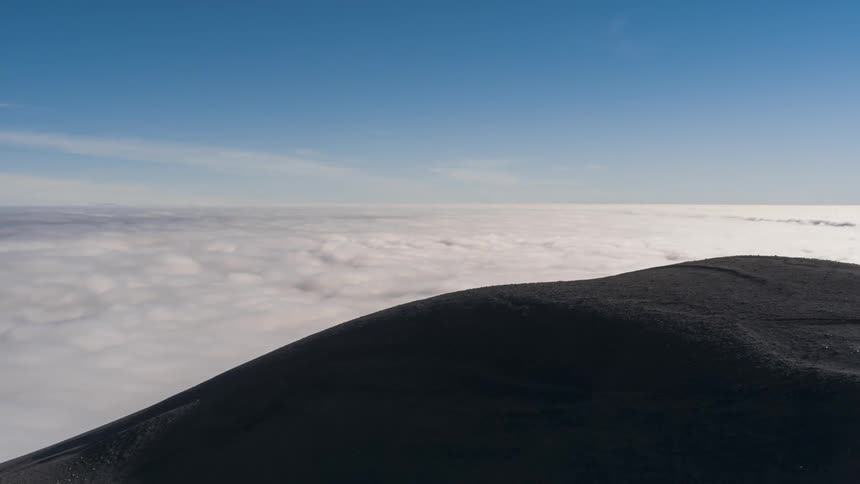 Time lapse of a sea of clouds rolling under mountain peak and a blue sky