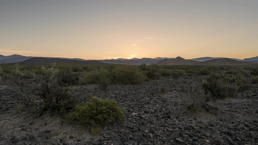 The sun is setting in the horizon of a desert