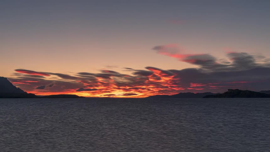Time lapse of clouds rolling over the ocean with mountains on the horizon