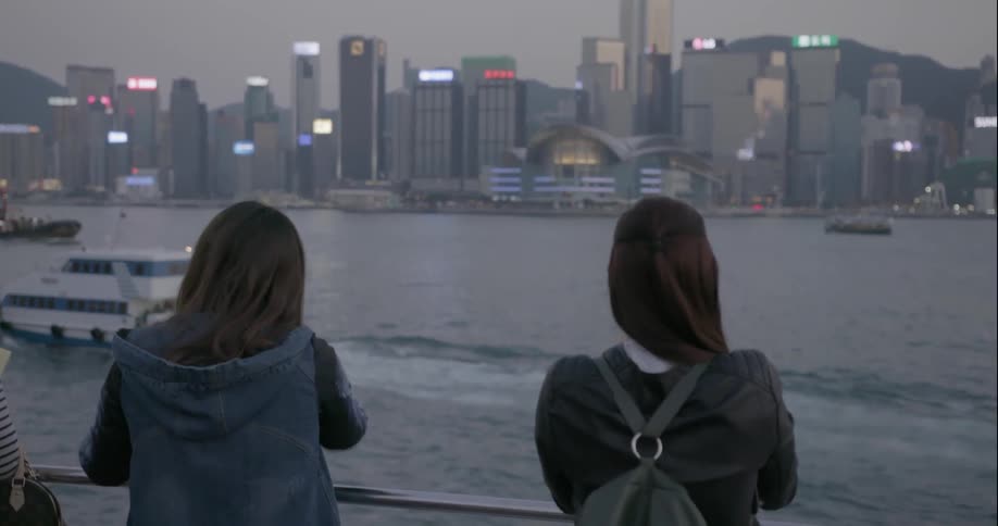 Two women photographing and observing large city from across a bay
