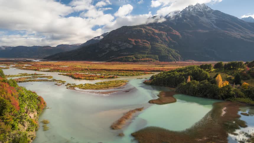 Greenish lake surrounded by mountains with clouds passing by