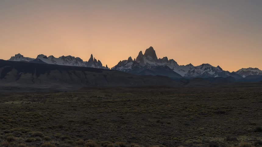 Sun sets behind mountain range bordering grassland