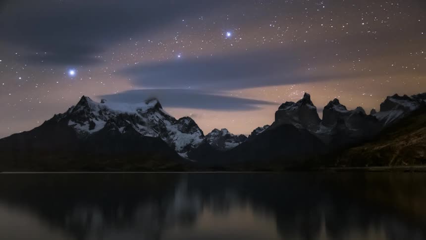 Night landscape with towering mountains under a starry sky reflected in a tranquil body of water
