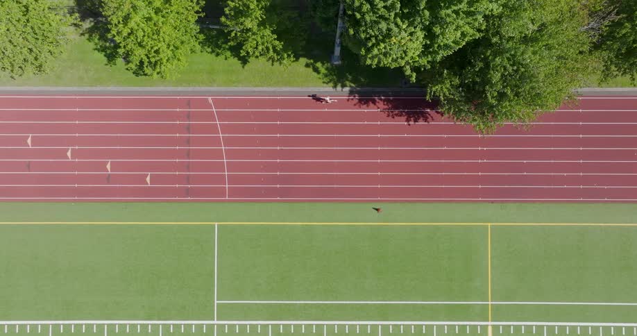 A lone athlete runs in the outer lane of an outdoor running track
