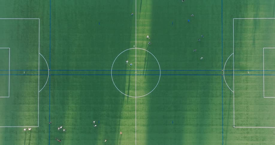 Birds eye view of two teams playing ultimate frisbee on a soccer field raked by the evening sun