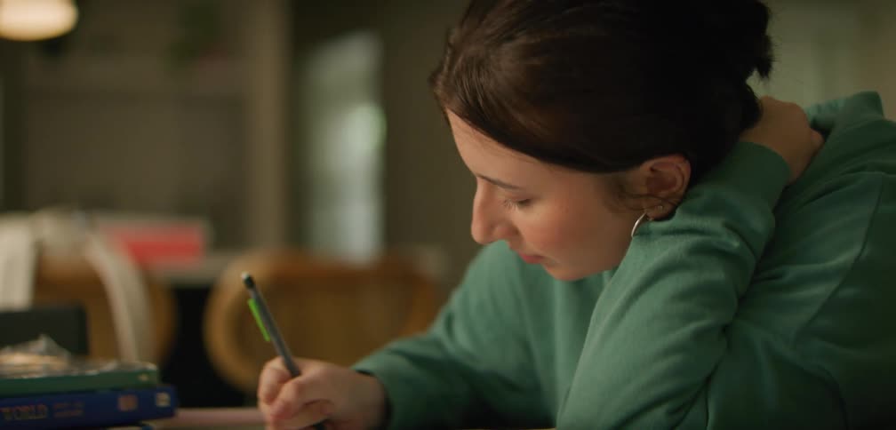 A young woman sitting writing with study books beside her
