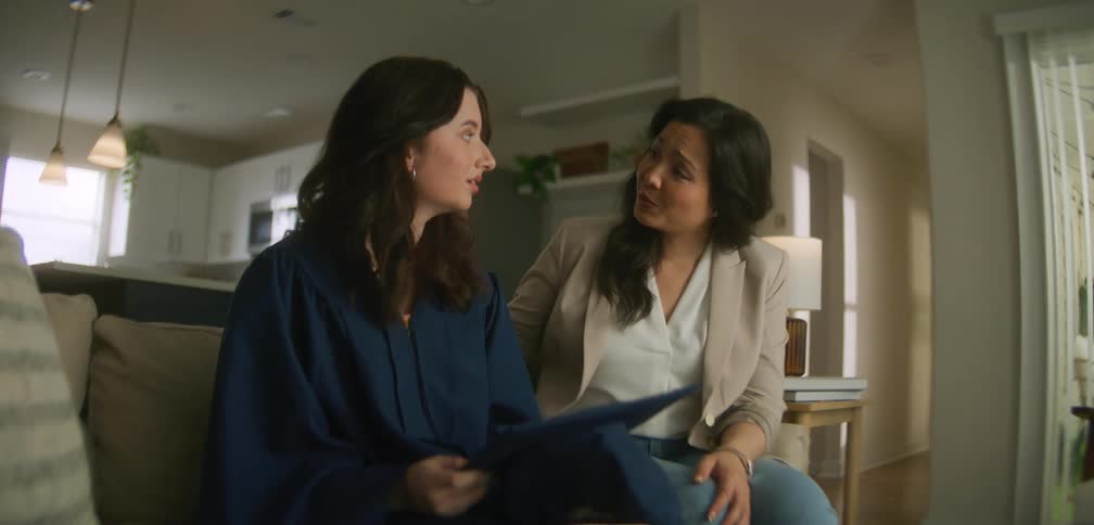 Daughter contemplating her graduate cap talks to her mother in their living room