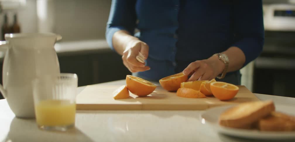 A woman cuts an orange into quarters on a chopping board