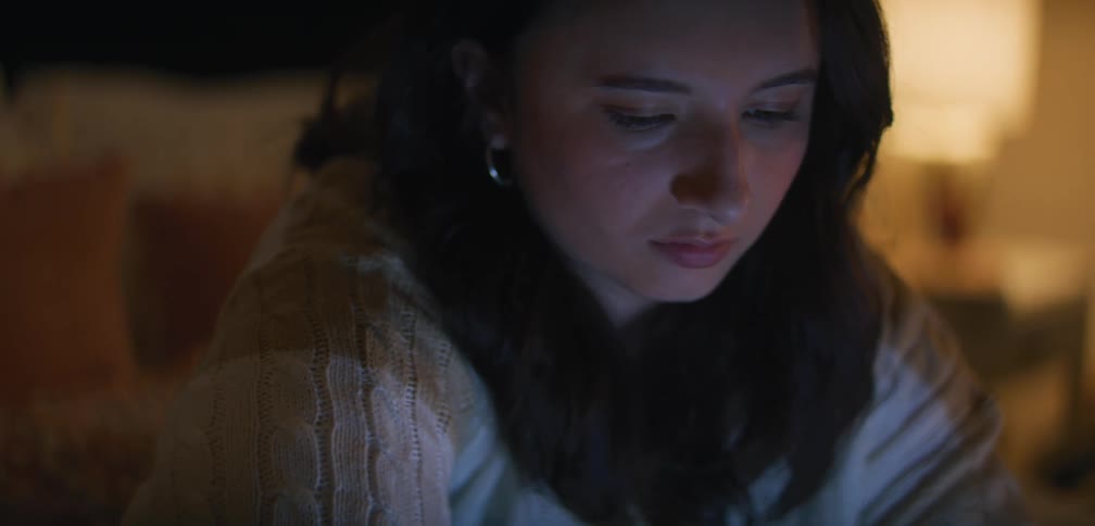 A young female working on a laptop in a dimly lit bedroom