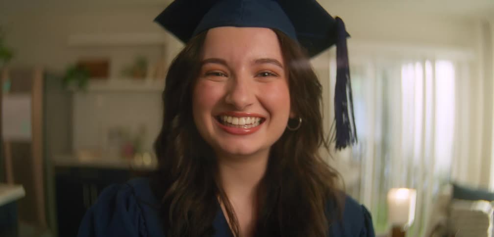 A happy young woman wearing a graduation cap smiles for the camera