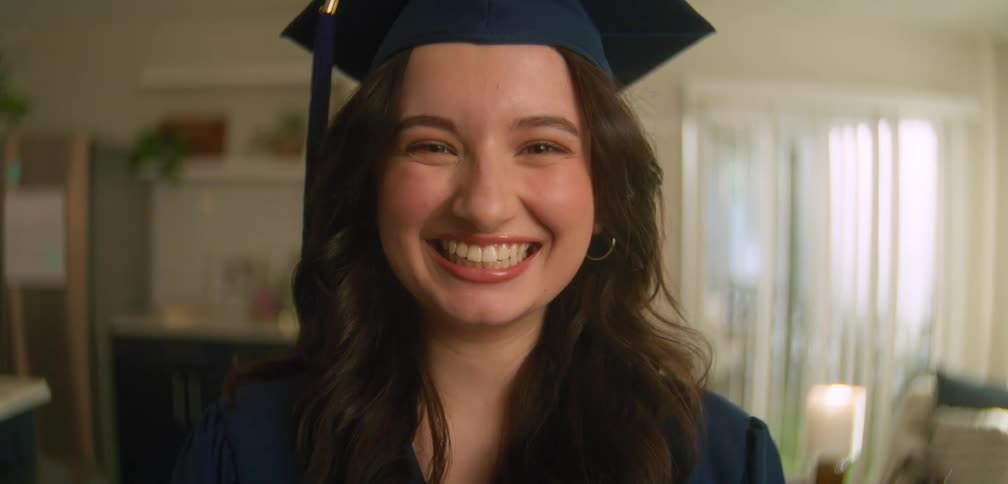 A female is smiling at the camera while wearing a graduation outfit