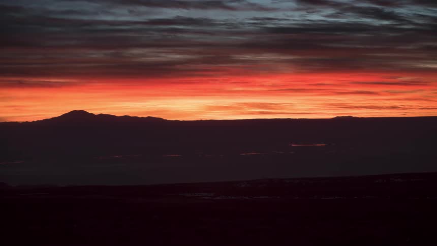 Sun setting behind the silhouette of mountains on a cloudy day