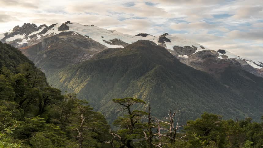 Mountainous landscape with snowcapped peaks in the background and wooded slopes in the foreground