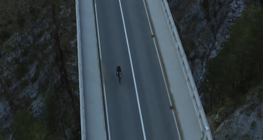 A man is biking on an empty road near the forest