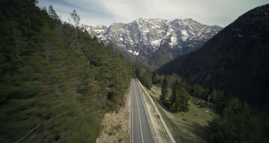 Vehicle drives along highway passing through forested mountains on route to a bridge over a gulch