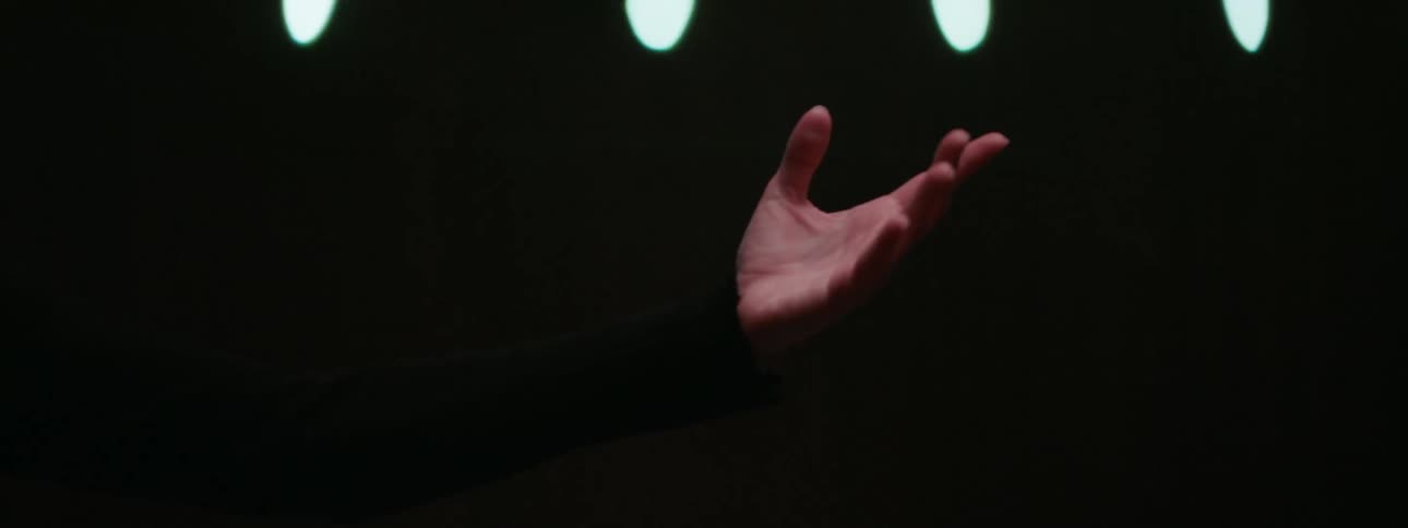 Male conductor holds out one hand while conducting an orchestra