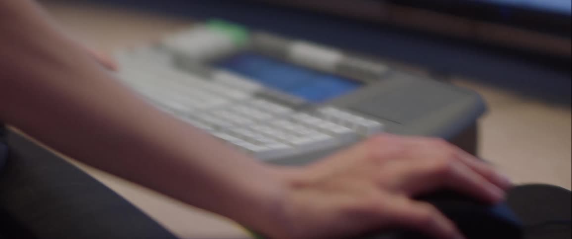 A person uses the keyboard and mouse on a control room with multiple screens