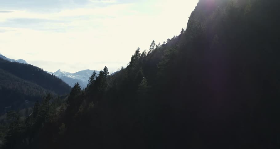 Aerial panorama of mountains with the silhouette of conifers and the reflection of sunlight