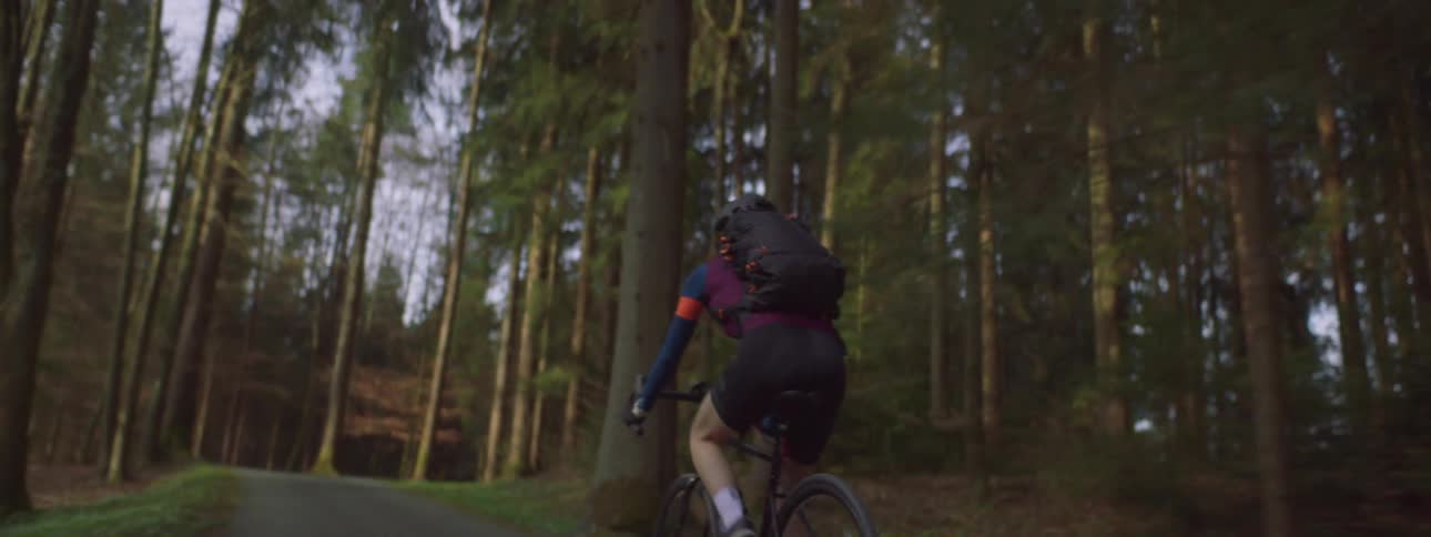 A person with a backpack riding a bicycle on a path through a forest