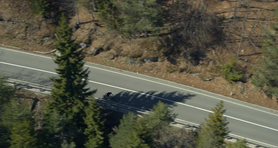 Aerial view of a winding road through a forested area and an isolated cyclist