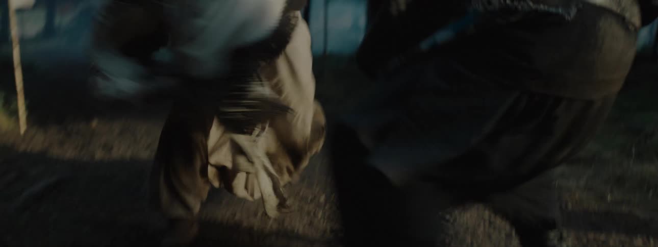 Two people wearing older style clothing fight in the woods