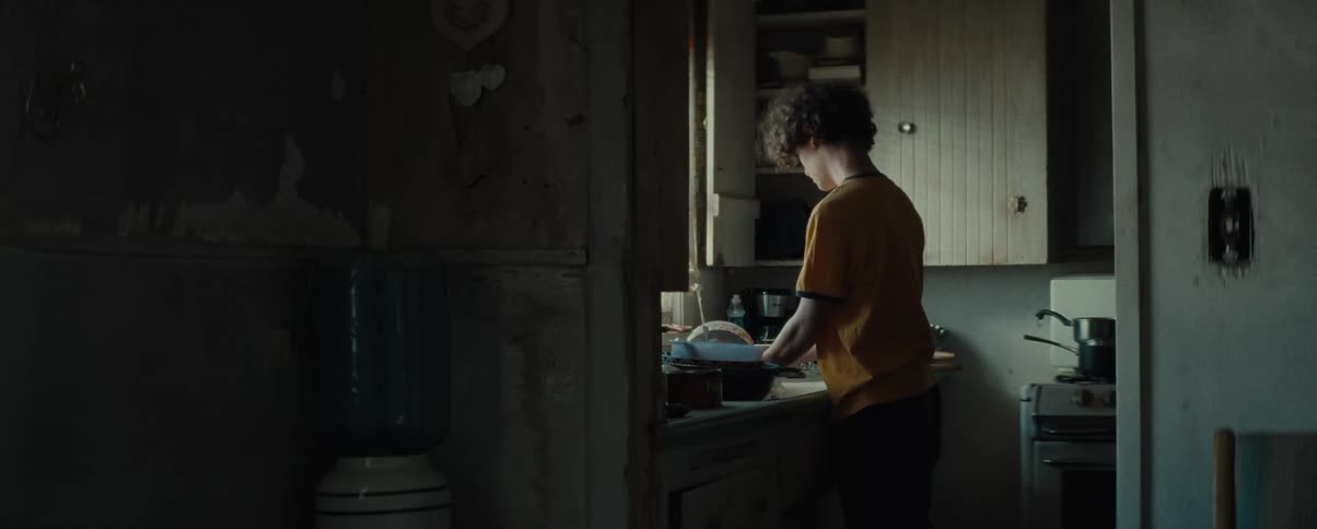 A young man washes dishes in the kitchen sink