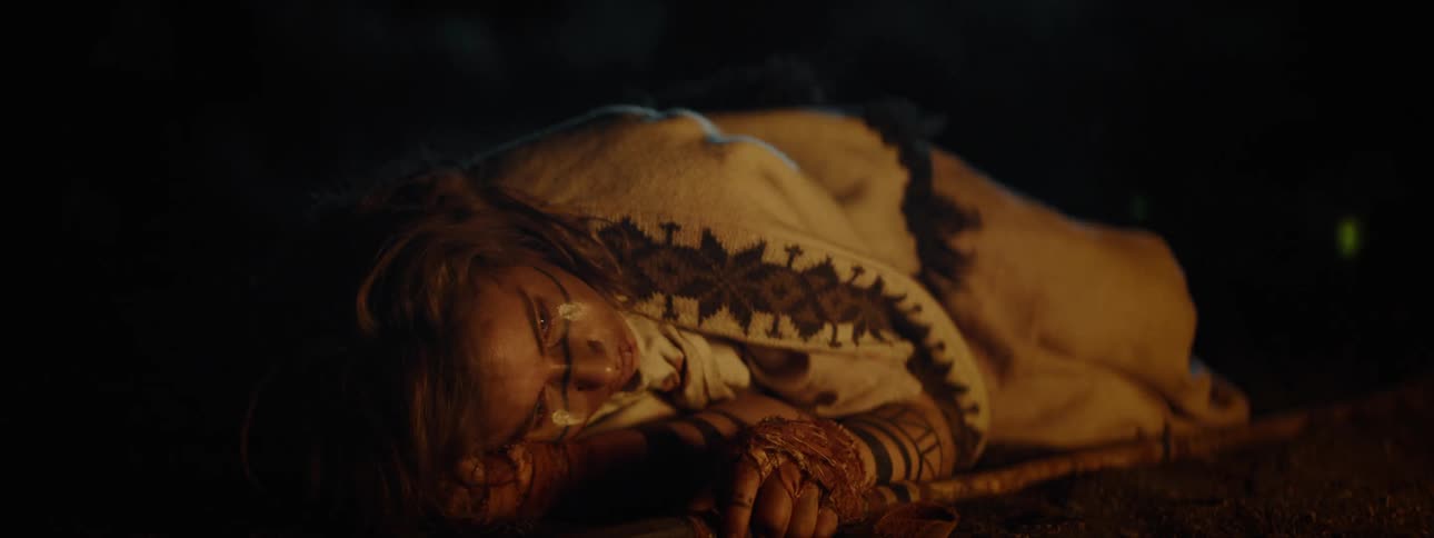 Person in a white cloak lying in the forest with reflections of a bonfire at night