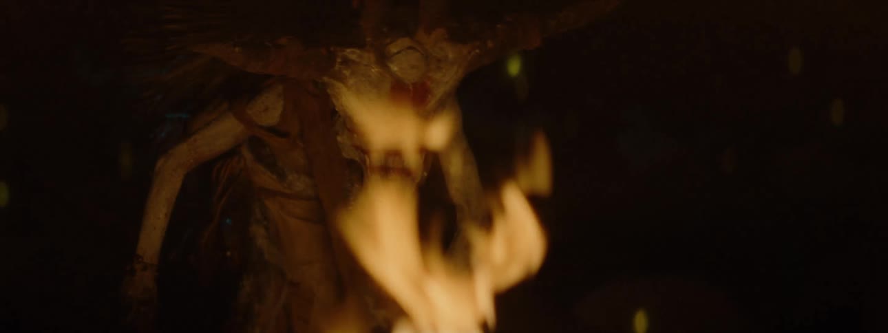 An ugly alien creature stands up near a roaring fire