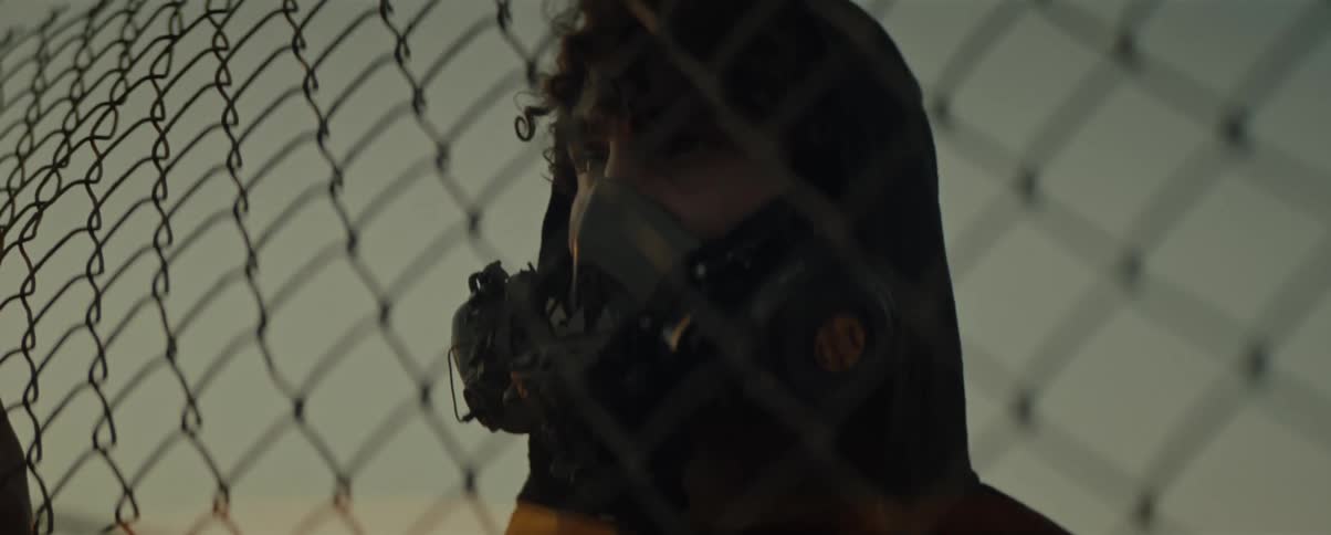 Youth wearing a breathing mask stands staring through a chain link fence